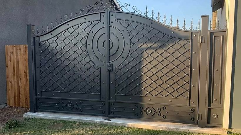 A tall double driveway gate in black iron: diamond lattice, a round centre medallion and spear finials along the arched top