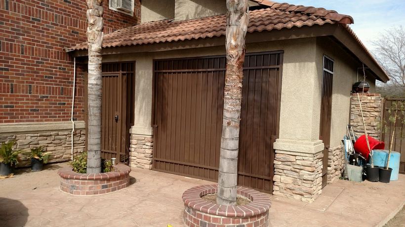 Brown iron security doors and a barred window on a stucco house with a tile roof